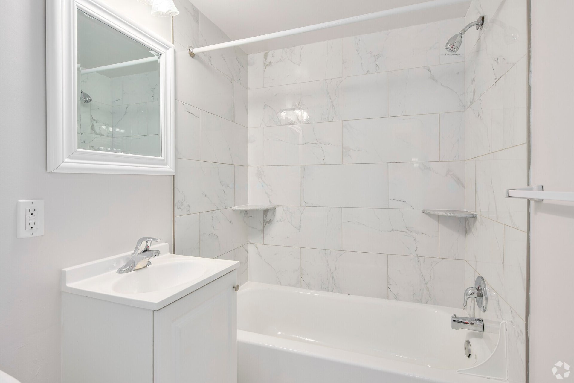 One-bedroom bathroom with white vanity and tiled tub surround
